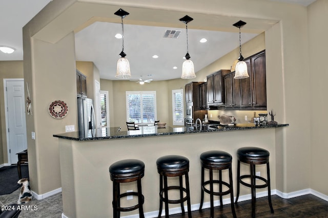 kitchen with pendant lighting, dark stone counters, dark hardwood / wood-style floors, dark brown cabinets, and kitchen peninsula