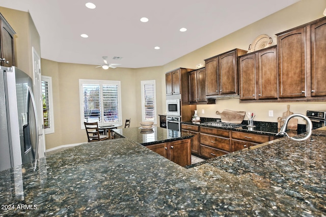 kitchen with appliances with stainless steel finishes, dark stone counters, dark brown cabinets, ceiling fan, and sink