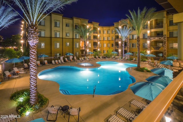 pool at night featuring a patio and a community hot tub