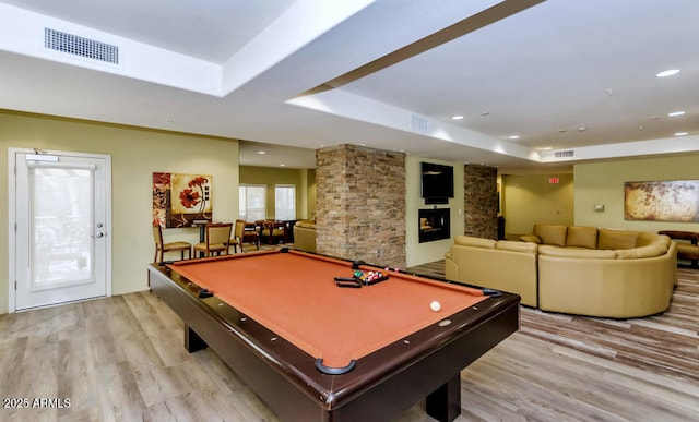 rec room featuring pool table, a large fireplace, a tray ceiling, and light hardwood / wood-style flooring