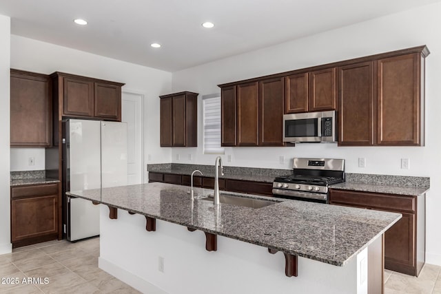 kitchen with a kitchen island with sink, a kitchen breakfast bar, sink, dark stone countertops, and stainless steel appliances