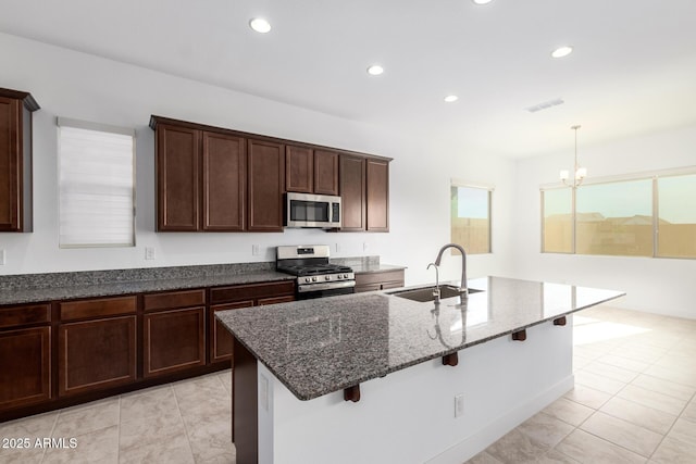 kitchen with stainless steel appliances, dark stone counters, an island with sink, sink, and a breakfast bar area