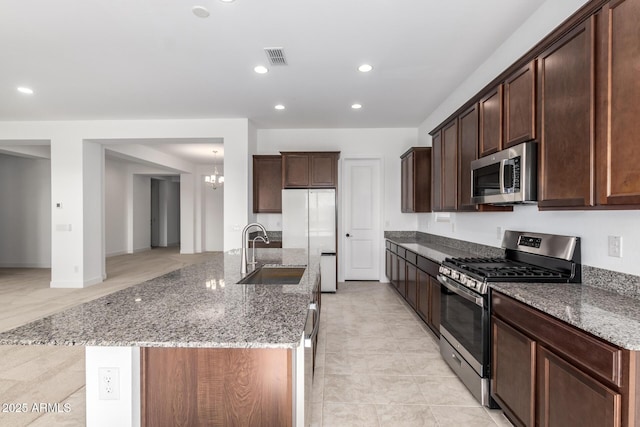 kitchen featuring sink, stainless steel appliances, a kitchen island with sink, and stone counters