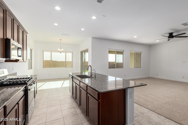 kitchen with light carpet, hanging light fixtures, appliances with stainless steel finishes, sink, and a center island with sink