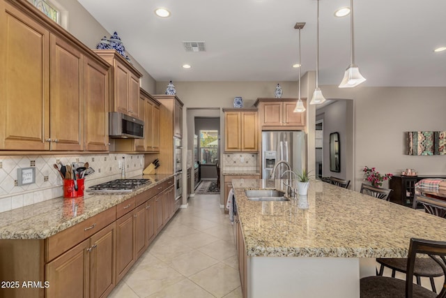 kitchen featuring a center island with sink, appliances with stainless steel finishes, tasteful backsplash, pendant lighting, and sink