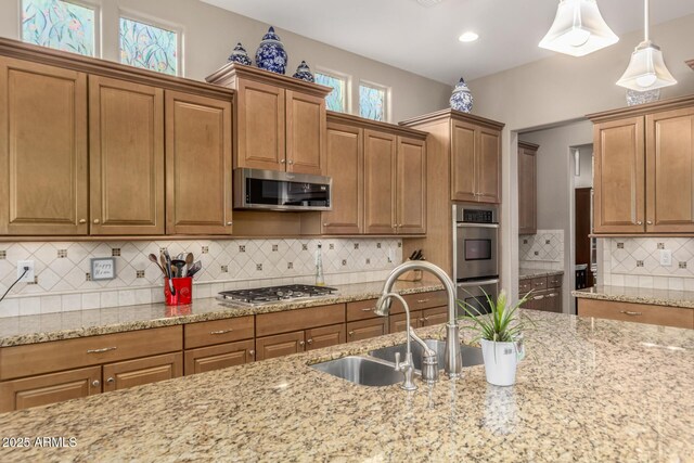 kitchen with appliances with stainless steel finishes, decorative backsplash, pendant lighting, light stone counters, and sink