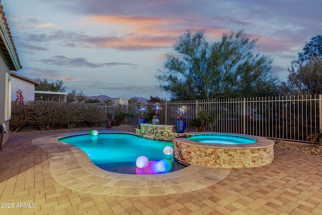 pool at dusk with a patio area and an in ground hot tub