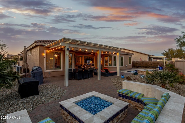 back house at dusk with a pergola, a patio area, and an outdoor living space with a fire pit