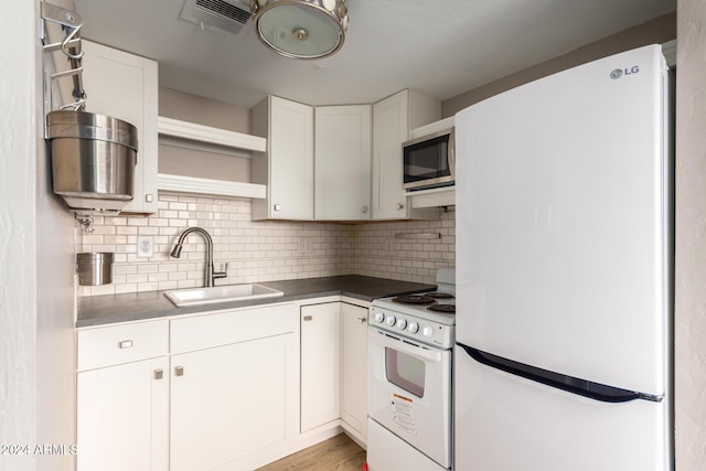 kitchen featuring fridge, sink, white cabinets, white stove, and decorative backsplash