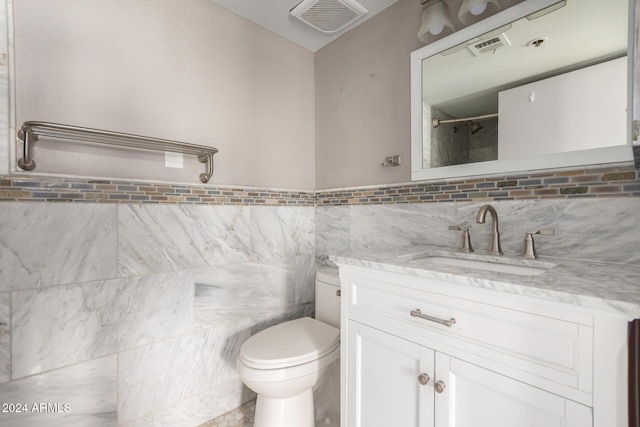 bathroom featuring toilet, vanity, and tile walls