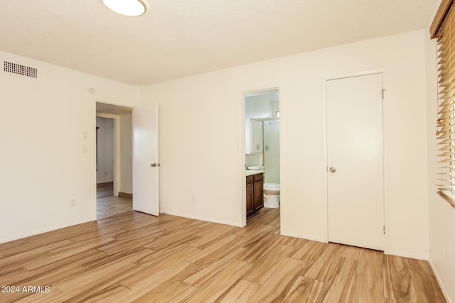 unfurnished bedroom featuring ensuite bath and light hardwood / wood-style flooring