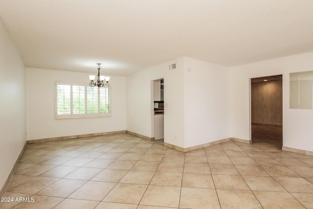 tiled empty room featuring a textured ceiling and a chandelier