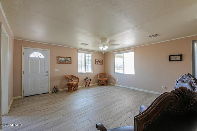 foyer entrance with ceiling fan, ornamental molding, light hardwood / wood-style floors, and a textured ceiling