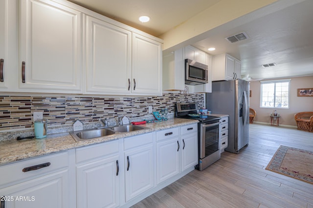 kitchen with sink, light hardwood / wood-style flooring, white cabinetry, stainless steel appliances, and decorative backsplash