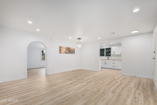 unfurnished living room featuring light wood-style floors, arched walkways, and baseboards