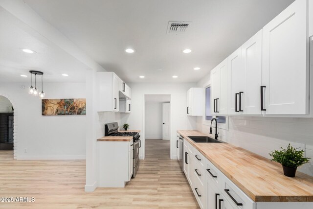 kitchen with decorative backsplash, light wood-style floors, gas stove, a sink, and butcher block countertops