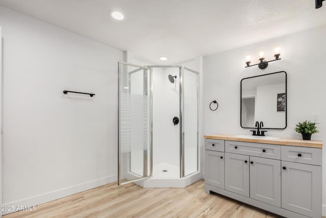 full bath featuring a stall shower, wood finished floors, vanity, and baseboards