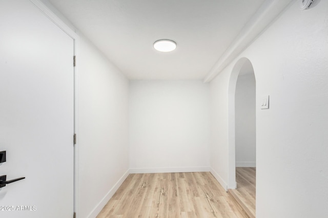 corridor featuring light wood finished floors, baseboards, and arched walkways