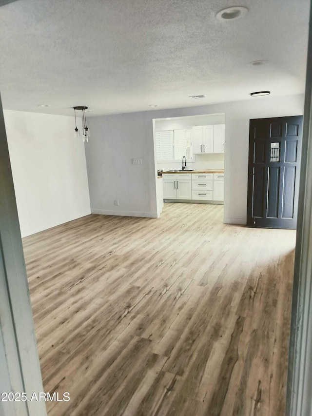 unfurnished living room with a textured ceiling, baseboards, a sink, and light wood-style floors
