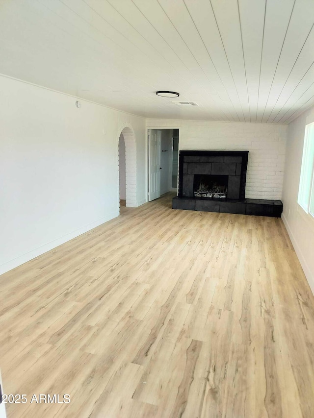 unfurnished living room featuring baseboards, arched walkways, wood finished floors, and a tile fireplace