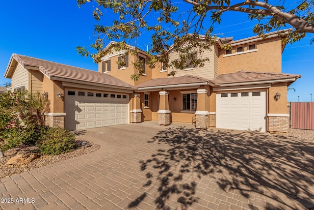 view of front facade with decorative driveway, stucco siding, an attached garage, stone siding, and a tiled roof