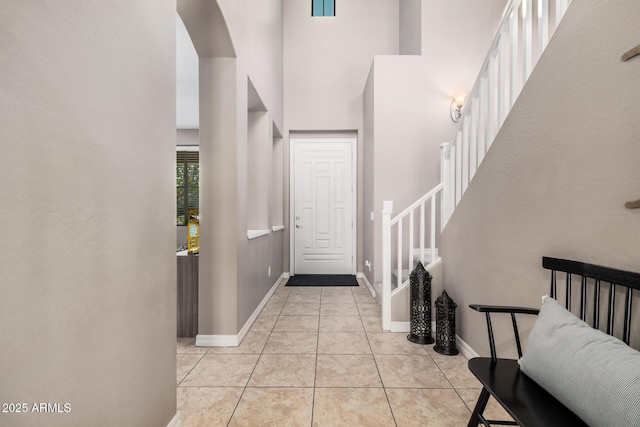 foyer with a towering ceiling, light tile patterned floors, stairs, and baseboards