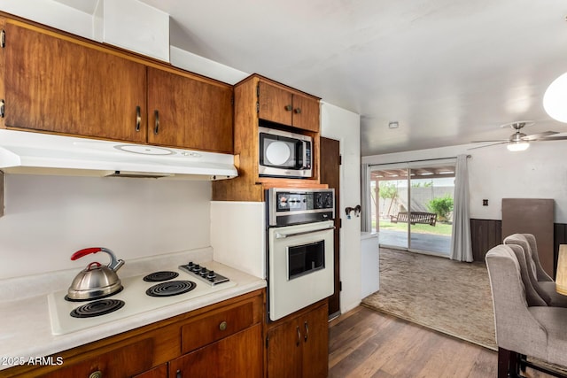 kitchen featuring white appliances, under cabinet range hood, light countertops, dark wood-style flooring, and brown cabinetry