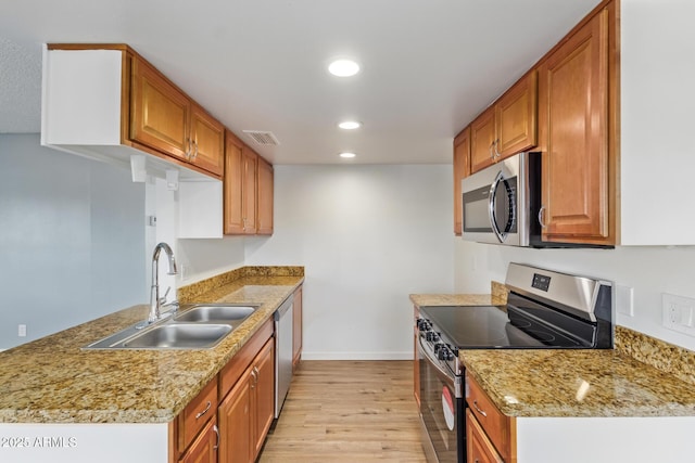 kitchen with light wood-type flooring, light stone countertops, sink, and stainless steel appliances