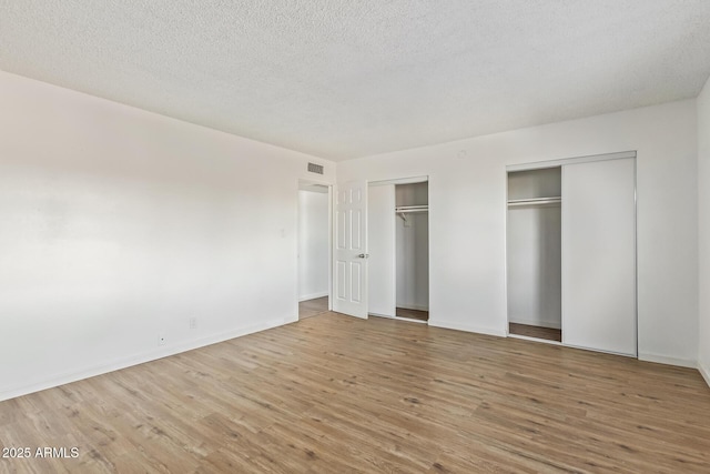 unfurnished bedroom with two closets, a textured ceiling, and hardwood / wood-style flooring