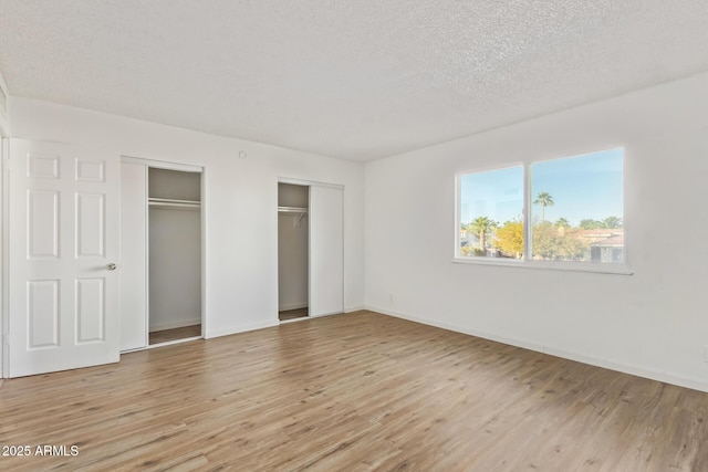 unfurnished bedroom with two closets, a textured ceiling, and light wood-type flooring