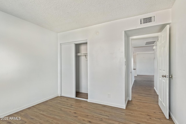 unfurnished bedroom with a textured ceiling, a closet, and hardwood / wood-style floors