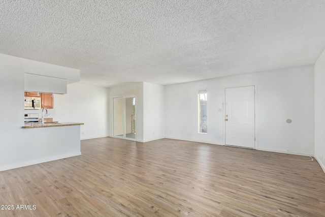 unfurnished living room with light hardwood / wood-style floors, sink, and a textured ceiling