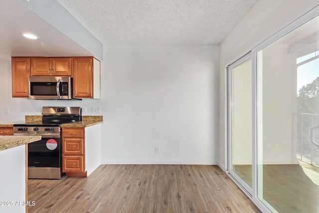 kitchen with a textured ceiling, stainless steel appliances, and light wood-type flooring