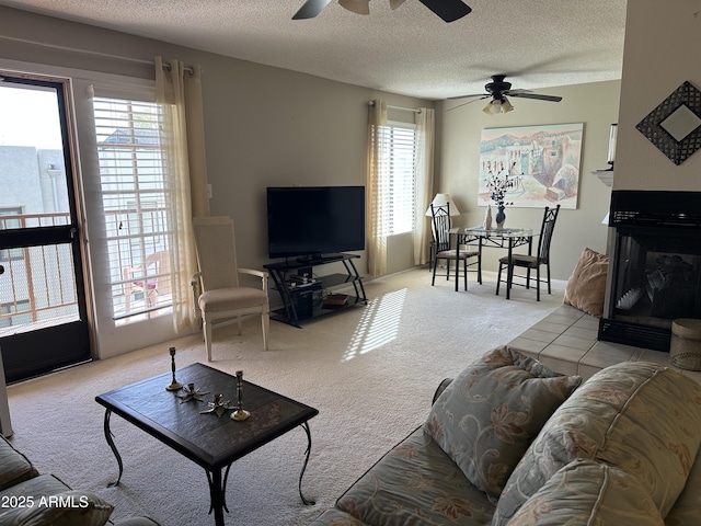 living room with a textured ceiling, carpet floors, a glass covered fireplace, and a ceiling fan