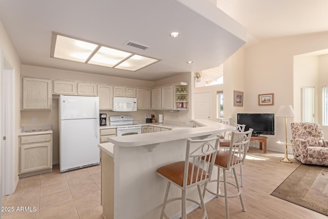 kitchen featuring sink, white appliances, a breakfast bar area, vaulted ceiling, and kitchen peninsula