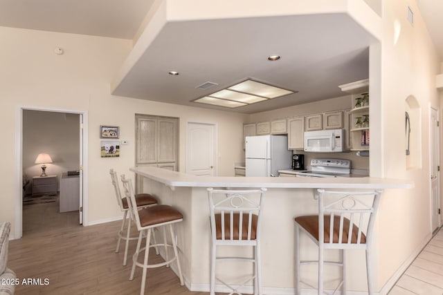 kitchen with a kitchen breakfast bar, light hardwood / wood-style flooring, white appliances, and kitchen peninsula