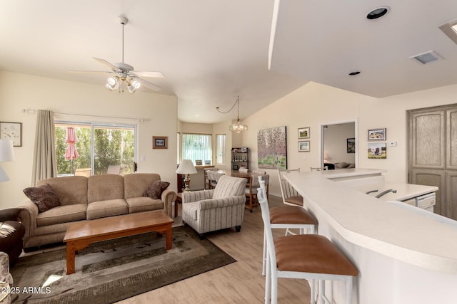 living room featuring ceiling fan with notable chandelier, vaulted ceiling, and light wood-type flooring