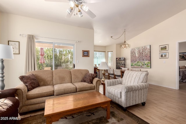 living room featuring hardwood / wood-style flooring, vaulted ceiling, ceiling fan with notable chandelier, and a wealth of natural light