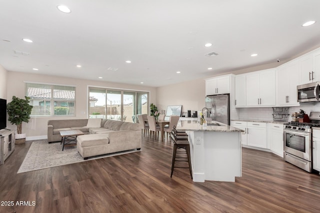 kitchen with white cabinetry, a breakfast bar area, stainless steel appliances, light stone countertops, and a center island with sink