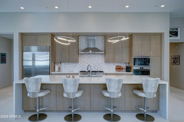 kitchen featuring wall chimney exhaust hood, built in appliances, and a breakfast bar