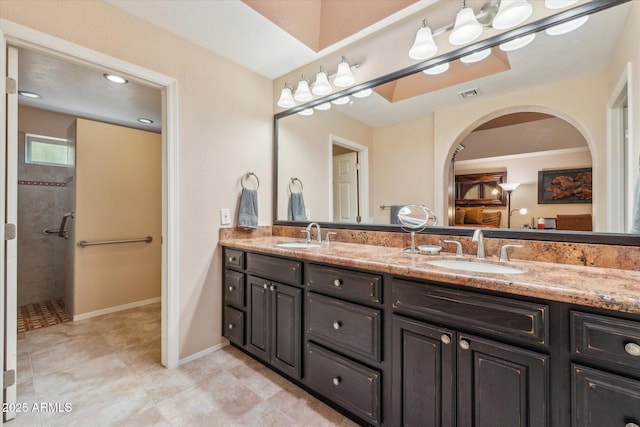 bathroom featuring double vanity, tiled shower, a sink, and visible vents