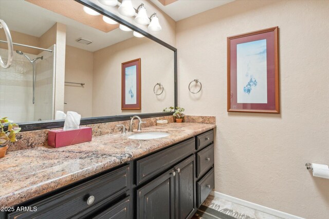 full bathroom featuring tiled shower, vanity, and baseboards