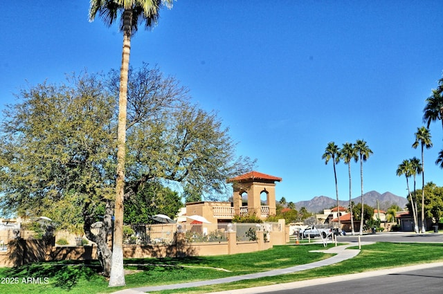 view of property's community with fence, a lawn, and a mountain view