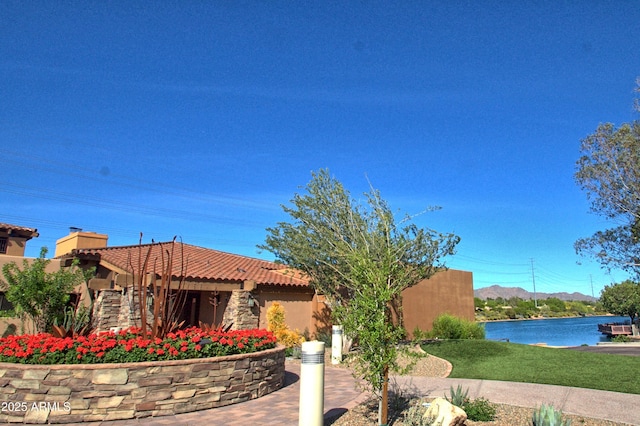 view of front of property featuring a tiled roof, a chimney, a water view, and stucco siding