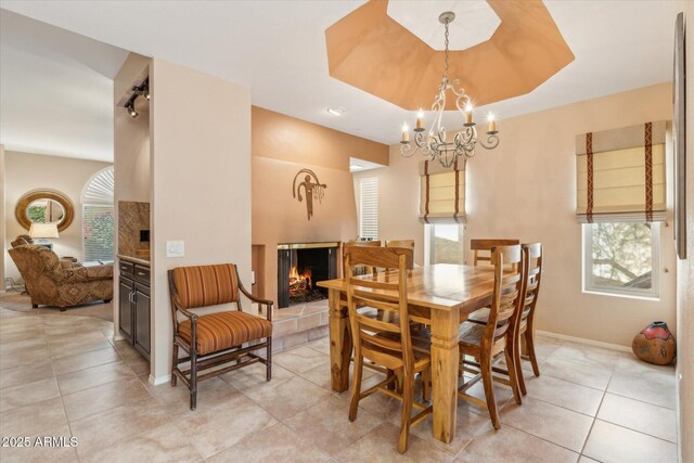 dining room featuring a tray ceiling, a healthy amount of sunlight, a multi sided fireplace, and light tile patterned flooring