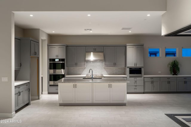 kitchen with stainless steel double oven, gray cabinets, a kitchen island with sink, and sink