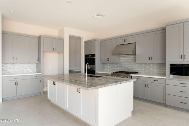 kitchen with backsplash, a center island with sink, sink, gray cabinets, and appliances with stainless steel finishes