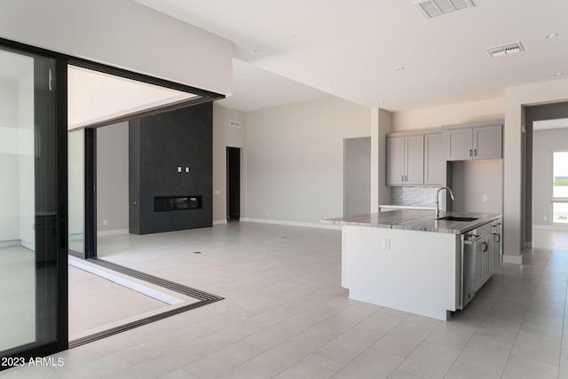 kitchen featuring tasteful backsplash, a kitchen island with sink, sink, dishwasher, and gray cabinets