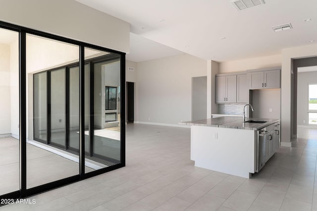 kitchen featuring sink, stainless steel dishwasher, an island with sink, gray cabinets, and decorative backsplash