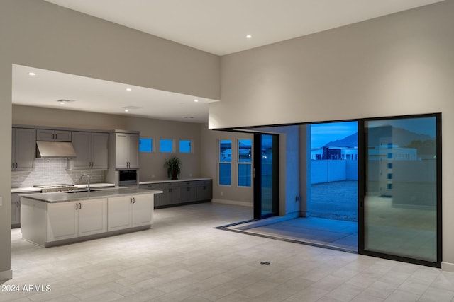 kitchen featuring stainless steel gas stovetop, backsplash, oven, gray cabinets, and an island with sink